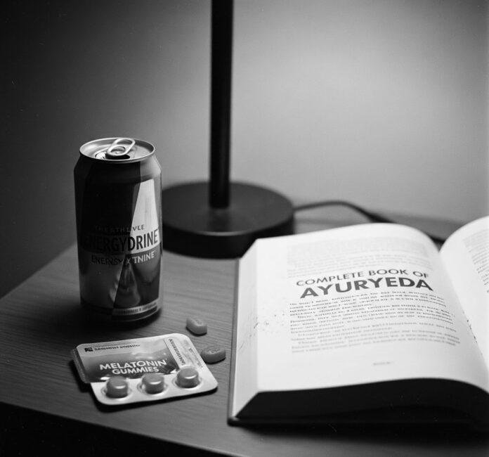 Nightstand with melatonin, energy drink, and dusty Ayurveda book.